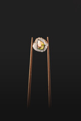 bacchette che reggono un roll di sushi su sfondo scuro