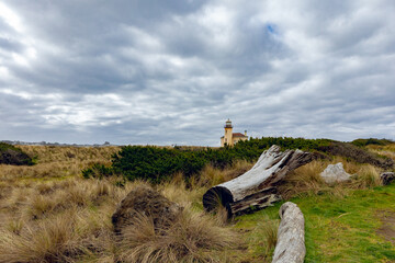 Dramatic moody blue sky landscape near Bandon Beach Oregon, with Coquille River Lighthouse in background and logs and grass in foreground.