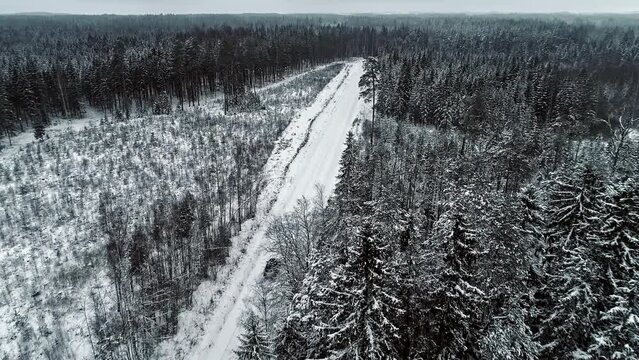 Car drives on rural track through white snowy forested landscape; drone
