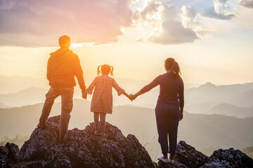 Silhouette family holding hands enjoying sunset sky on top mountain.