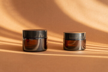 Two jars of amber glass for cosmetics on brown background with shadow in form of stripes. Mock-ups...