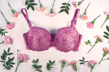 Beautiful lace purple pink bra surrounded by flower frame, white background, top view. Stylish lingerie, underwear.