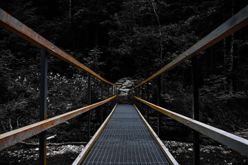 Suspension bridge in the forest with a dark background. Leading lines photography of a metal bridge.