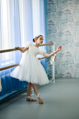 A beautiful girl ballerina in a white dress is engaged at the stonk. She's in a dance studio....