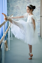 A beautiful girl ballerina in a white dress is engaged at the stonk. She's in a dance studio....