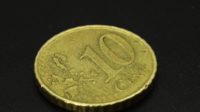 Golden ten cents coin rotating on a black surface, macro shot in 4k extreme detail close up view.
