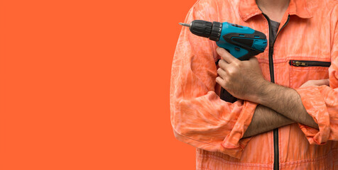 Chief mechanic wearing an orange uniform dress holding blue electric drill in front of orange background.  Portrait with studio light.