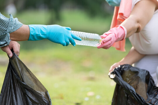 close up volunteer hands picking up plastic bottle and putting garbage bag in the park