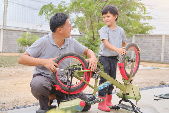 Asian Father And Son Spend Time Together, Dad And Son Playing And Repairing Bicycle Wheel, Fixing Bike With Spanner In Sunny Summer Day Outdoor On Nature At Home Backyard, Selective Focus At Kid