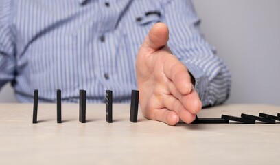 Domino effect stopping. Businessman hand closeup protecting domino pieces from falling. Successful...