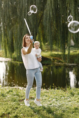 Young mother holding her little daughter in a hands and blow a soap bubbles