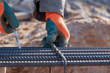 A worker uses steel tying wire to fasten steel rods to reinforcement bars. Close-up. Reinforced concrete structures - knitting of a metal reinforcing cage.