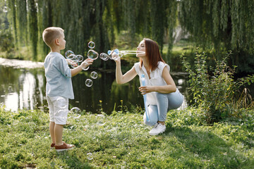 Young mother resting with her son in a park and blowing a soap bubbles