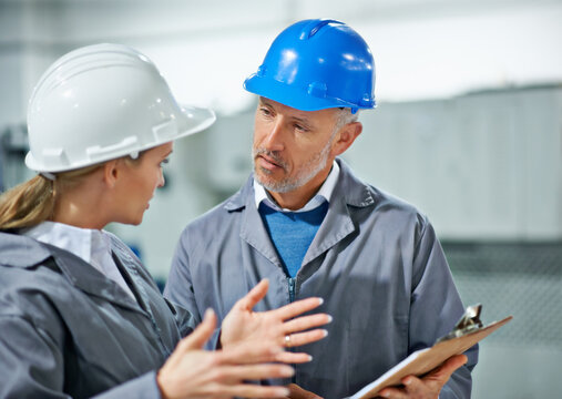 Communication takes practice. Two factory employees wearing hardhats having a discussion.