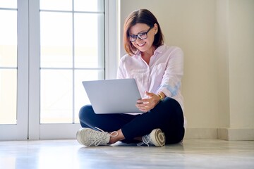 Middle aged woman sitting on floor using laptop
