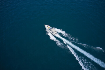 Modern boat in motion making a trail on the water top view. One boat on blue water drone view. Boat moving fast aerial view.