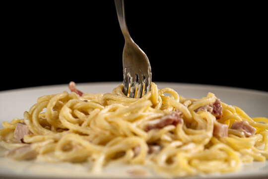 Fork Is Spinning Carbonara Spaghetti On White Plate On Black Background