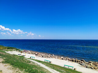 Seascape with coastline with empty benches, stone mound and deep blue sea on a sunny summer day. City beach in the city of Henichesk. Sea shore line with water surface. View point.