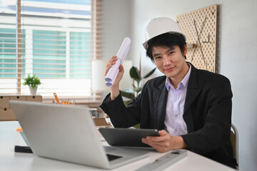 Confident Architect male in hard hat holding digital tablet and blueprint in his hand.