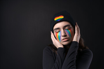 Portrait young crying woman with painted LGBT flag on her cheek. Crying with rainbow in black hat...
