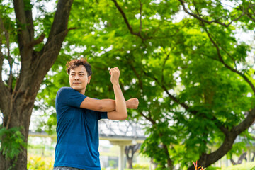 Asian man in sportswear and smartwatch stretching body while jogging at public park in the city in the morning. Healthy male athlete enjoy outdoor lifestyle sport training workout running exercise