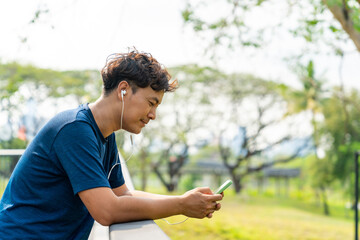 Asian man listening to music from earphones and smartphone application while jogging at city park i summer morning. Healthy male athlete enjoy outdoor sport training workout exercise and running