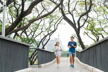 Happy family Asian couple in sportswear jogging exercise together at city public park in summer morning. Healthy man and woman enjoy outdoor lifestyle activity sport training fitness running workout