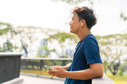 Asian man listening to music from earphones and smartphone application while jogging at city park i summer morning. Healthy male athlete enjoy outdoor sport training workout exercise and running - Powered by Adobe