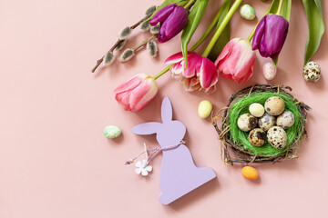 Pink and purple tulips with colorful quail eggs in a nest over pink background. Spring and Easter holiday concept. Top view flat lay.