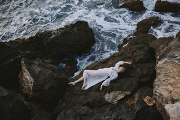 sensual woman in a secluded spot on a wild rocky coast in a white dress landscape