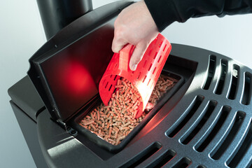 Close-up on pellets, black domestic pellet stove, man loading by hand granules with a red 3 d...