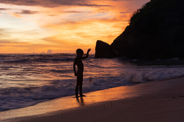 Fototapeta premium Child boy on the ocean at sunset, happy childhood, unity with nature, harmony.