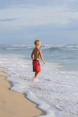 Fototapeta premium A child on the beach plays in the waves of the ocean. Boy on the ocean, happy childhood. tropical life.