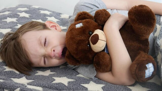 A pretty boy lay down to sleep hugging his teddy bear
