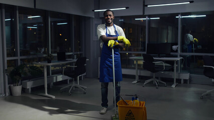 Portrait of African-American janitor smiling at camera in dark empty office