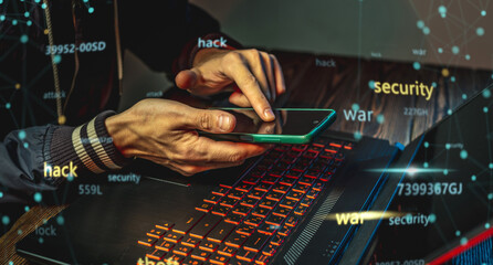 A hacker with a phone is typing with his hands on a laptop keyboard in a dark room. Cyber warfare and Dos attacks
