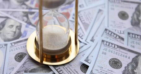 Sand timer clock with sparkling white sand and a person putting 100 dollar American banknotes. Concept: Saving money investing - Powered by Adobe