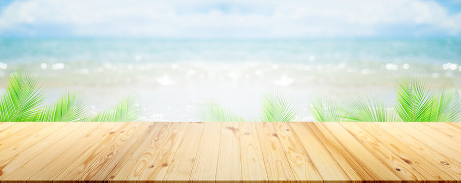 Table on sea with palm leaves background.empty desk wooden on blur blue ocean sand with bright whithe bokeh at coast. mockup counter bar montage on blurry water.tourism travel tropical summer holiday.