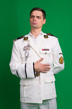 A marine captain wearing a white suit, standing half-turned, isolated on a green background.
