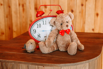 A teddy bear lying on a shelf next to a red alarm clock
