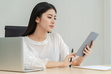 Beautiful Asian woman working on a desk for a laptop and a tablet.