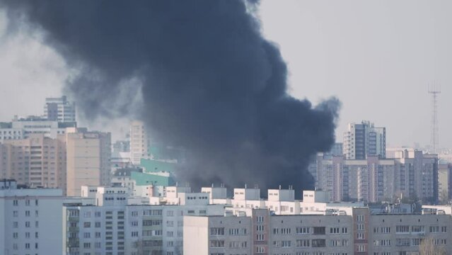 Aerial view of black puffs of thick acrid smoke from fire in dense high-rise building of large city. Fire, disaster on sunny summer day in town. 