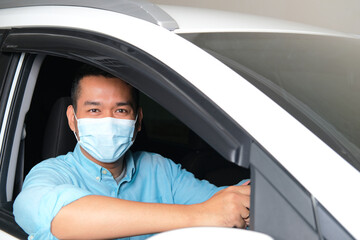 Adult Asian man wearing medical face mask and looking to the camera from inside his car