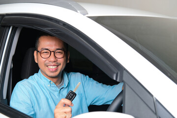 Adult Asian man smiling happy after buying a new car and showing the key - obrazy, fototapety, plakaty