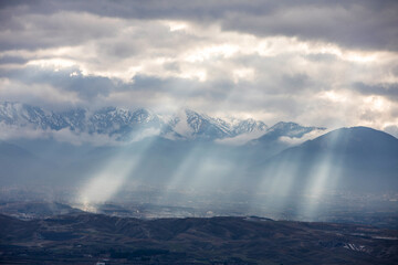 Sun light piercing through the clouds and hitting the mountains