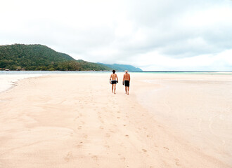 Where relaxation meets adventure. Rearview shot of two young men walking along the beach.
