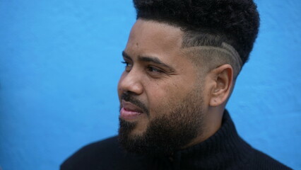 A pensive young man on blue background in street observing with modern haircut