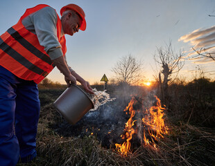 Fireman ecologist fighting wildfire in field with evening sky on background. Male environmentalist...