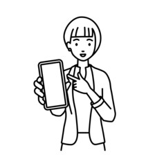 立ってスマートフォンを指差してこちらに向けて見せているジャケットの女性