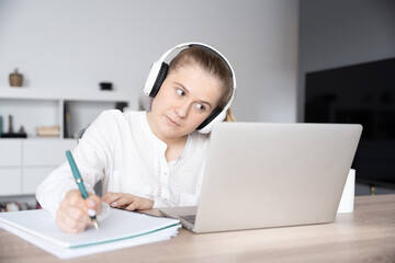 Female student taking notes on a notebook in front of a laptop during a virtual class